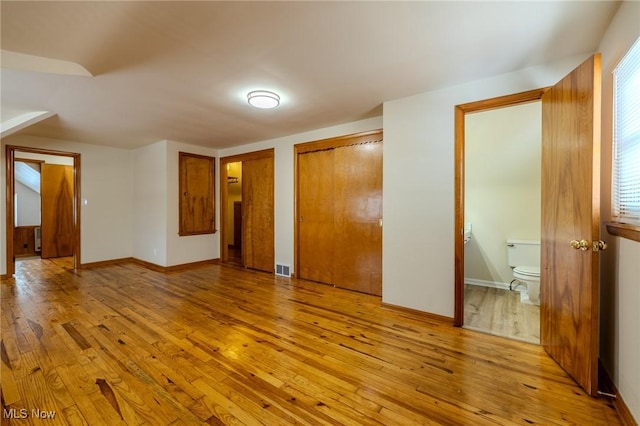 unfurnished bedroom with light wood finished floors, visible vents, baseboards, ensuite bath, and two closets