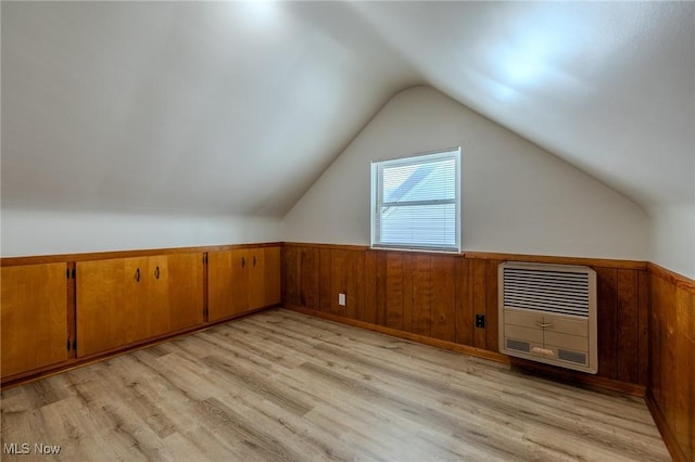 bonus room featuring a wainscoted wall, heating unit, light wood-style floors, vaulted ceiling, and wooden walls