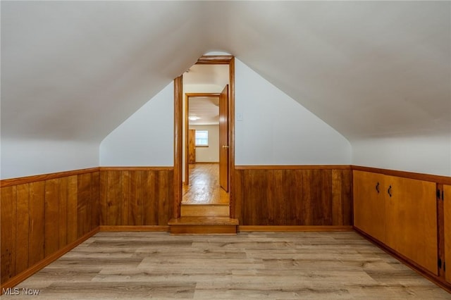 bonus room featuring a wainscoted wall, wood walls, vaulted ceiling, and light wood-style floors