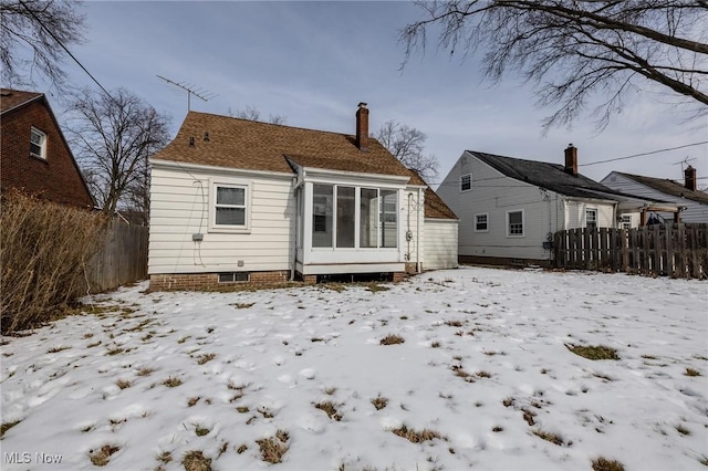 snow covered property featuring fence, a chimney, and a detached garage