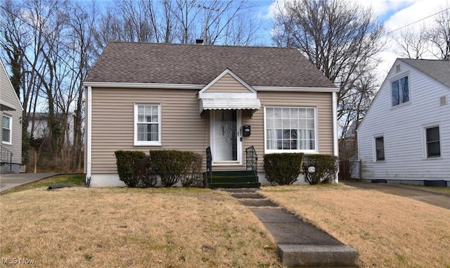 bungalow-style home featuring entry steps, a shingled roof, and a front yard