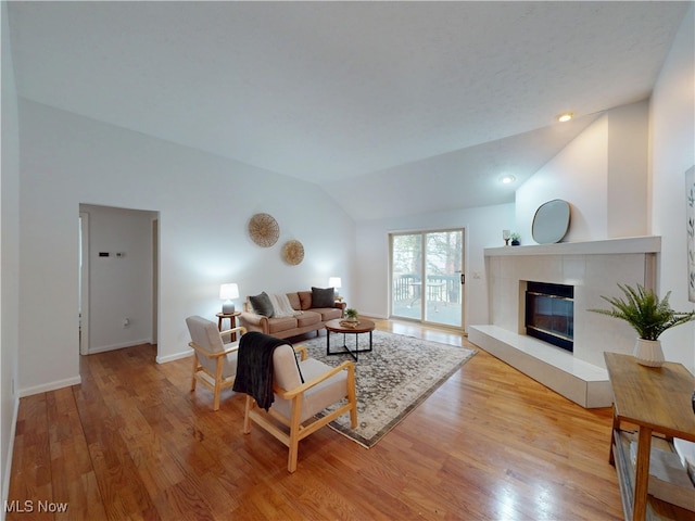 living area featuring lofted ceiling, light wood-type flooring, baseboards, and a tiled fireplace