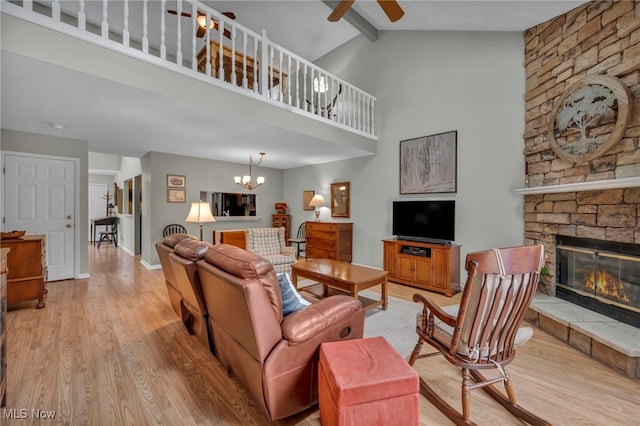 living room featuring ceiling fan with notable chandelier, a high ceiling, a fireplace, baseboards, and light wood finished floors