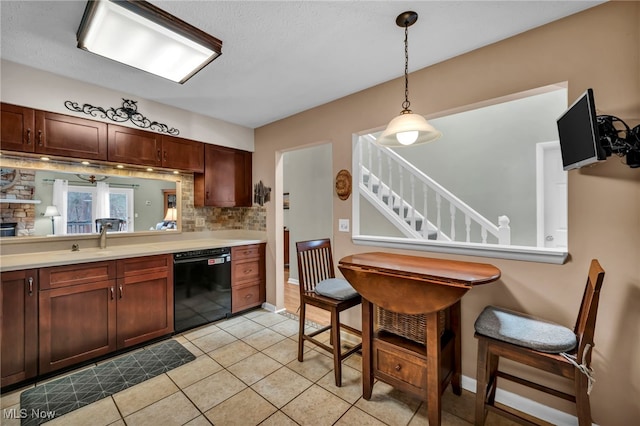 kitchen featuring dishwasher, light countertops, a stone fireplace, pendant lighting, and light tile patterned flooring