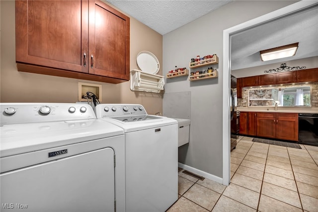 washroom with a textured ceiling, light tile patterned flooring, baseboards, cabinet space, and washing machine and clothes dryer