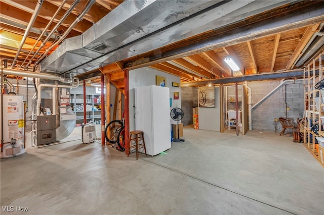 unfinished basement featuring gas water heater, freestanding refrigerator, and concrete block wall