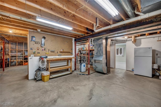 unfinished basement featuring a workshop area and freestanding refrigerator