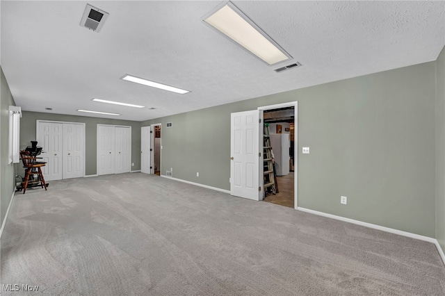 carpeted empty room featuring visible vents, a textured ceiling, and baseboards