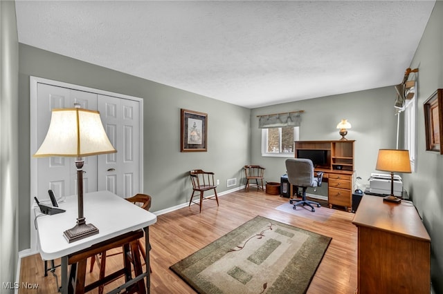 office space featuring light wood-type flooring, a textured ceiling, and baseboards