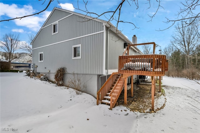 snow covered rear of property featuring a garage, a chimney, stairway, and a wooden deck