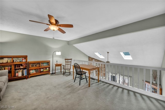 carpeted office space featuring vaulted ceiling with skylight and ceiling fan