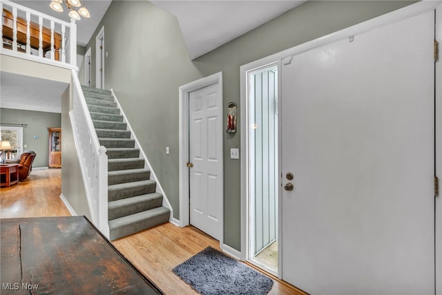 foyer entrance featuring a notable chandelier, stairs, baseboards, and wood finished floors