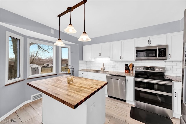 kitchen with stainless steel appliances, butcher block counters, a sink, visible vents, and tasteful backsplash