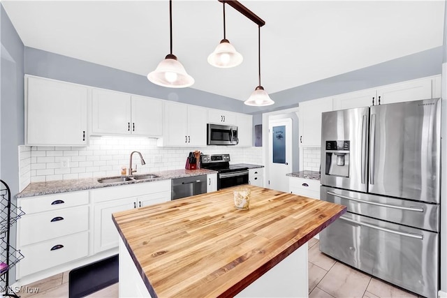 kitchen with appliances with stainless steel finishes, a sink, butcher block counters, and white cabinets