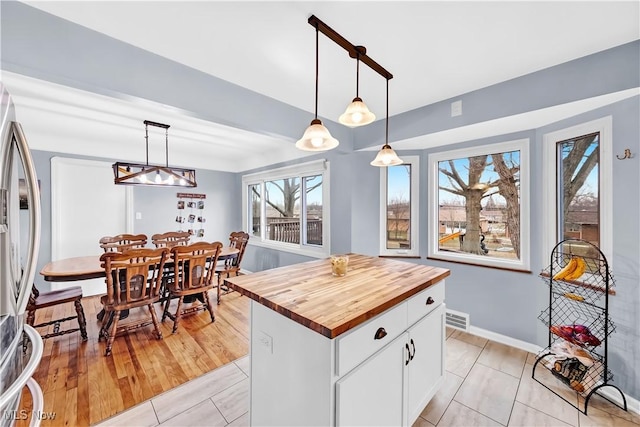 kitchen featuring stainless steel refrigerator with ice dispenser, visible vents, hanging light fixtures, white cabinetry, and wood counters