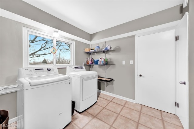 clothes washing area featuring laundry area, light tile patterned floors, baseboards, and washing machine and clothes dryer