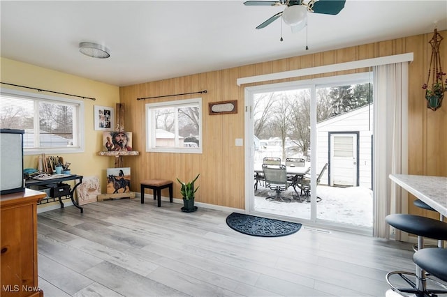 sitting room featuring ceiling fan, wood walls, light wood-style flooring, and baseboards