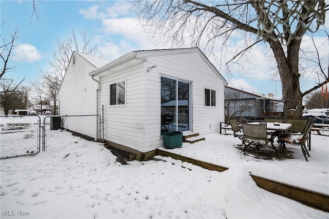 snow covered house featuring entry steps, a gate, fence, and outdoor dining space