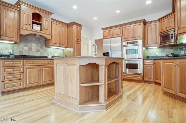 kitchen featuring a center island with sink, open shelves, stainless steel appliances, a sink, and light wood-type flooring