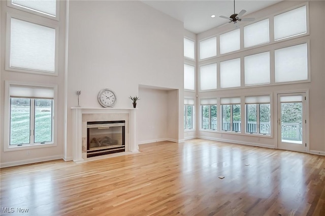 unfurnished living room with wood finished floors, ceiling fan, a high ceiling, and a premium fireplace