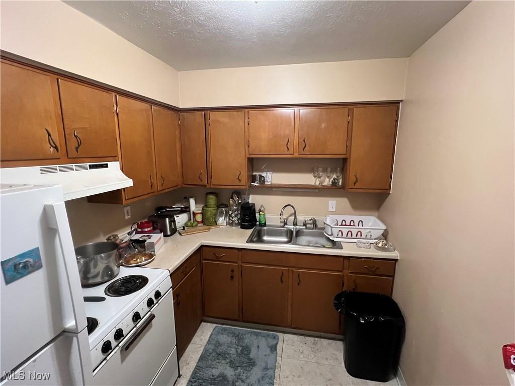 kitchen with white appliances, light countertops, under cabinet range hood, open shelves, and a sink