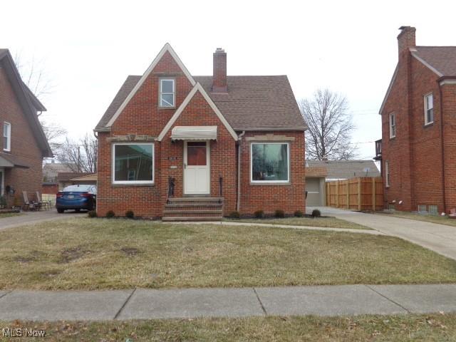 view of front of house with brick siding, a chimney, a front yard, and fence