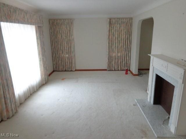 unfurnished living room featuring a fireplace with raised hearth, baseboards, carpet flooring, and a healthy amount of sunlight