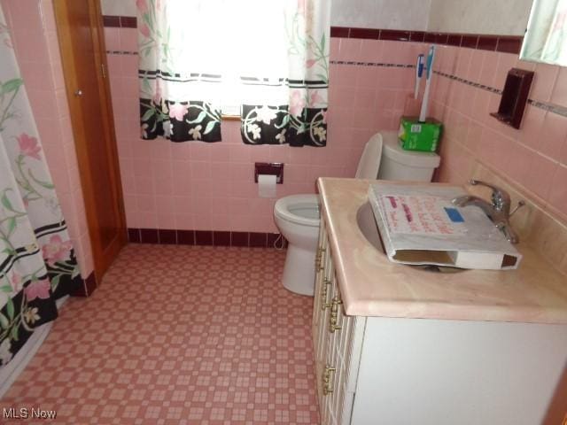 full bathroom with tile walls, vanity, toilet, and tile patterned floors