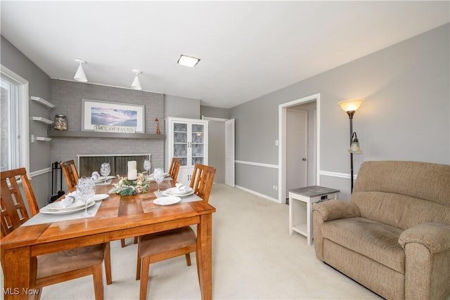 dining room with light carpet, a fireplace, and baseboards