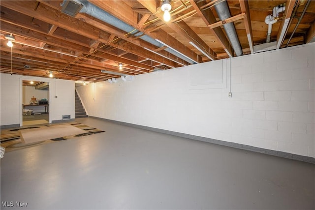 unfinished basement featuring stairway and concrete block wall