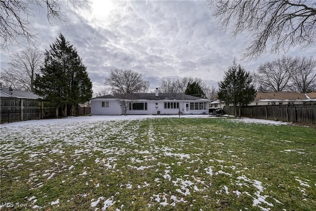 snow covered back of property with a fenced backyard and a yard