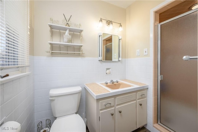 bathroom with toilet, vanity, tile walls, wainscoting, and a shower stall