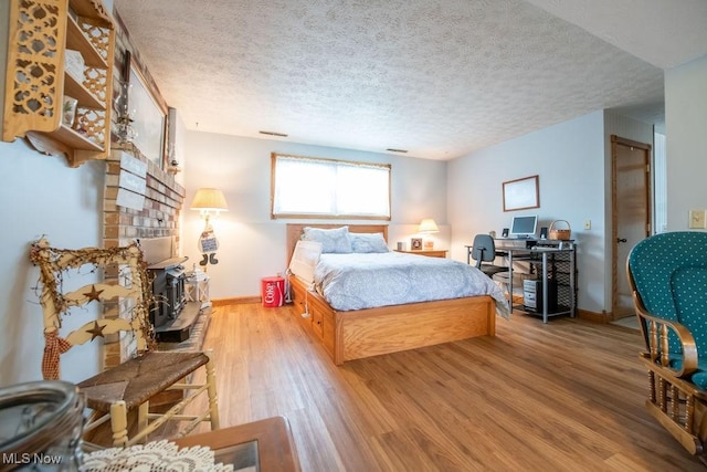 bedroom with visible vents, a textured ceiling, baseboards, and wood finished floors