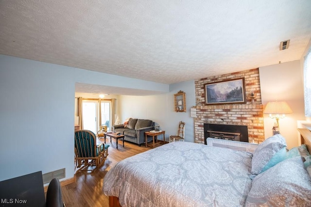 bedroom with a textured ceiling, a brick fireplace, wood finished floors, and visible vents