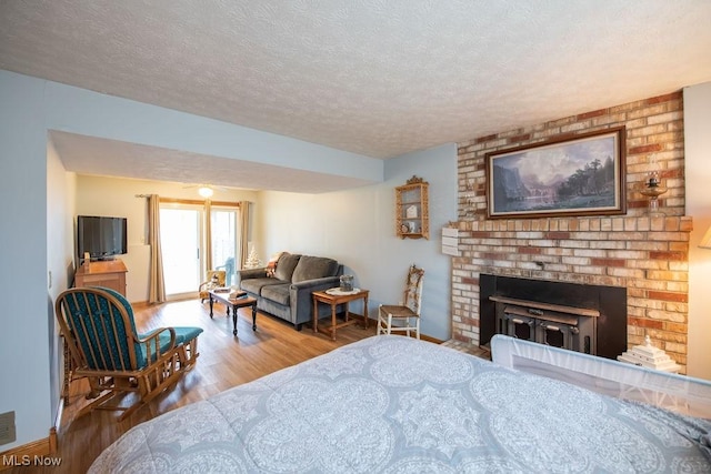 bedroom featuring a textured ceiling, a fireplace, wood finished floors, and baseboards