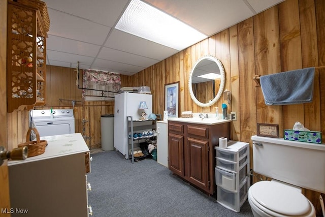 bathroom featuring washer and clothes dryer, toilet, wood walls, vanity, and a drop ceiling