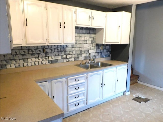 kitchen with light countertops, white cabinetry, a sink, and baseboards