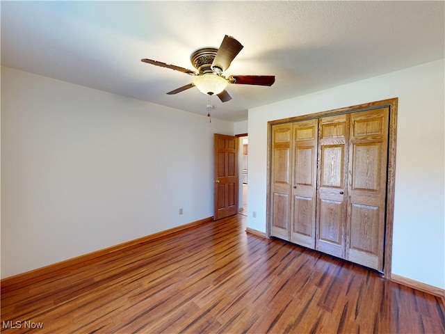 unfurnished bedroom featuring a closet, wood finished floors, a ceiling fan, and baseboards