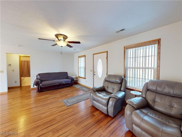 living room featuring a ceiling fan, light wood-type flooring, visible vents, and baseboards