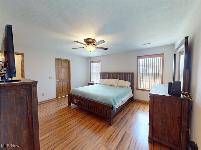 bedroom with visible vents, baseboards, a ceiling fan, light wood-style flooring, and a textured ceiling