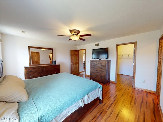 bedroom featuring light wood finished floors, visible vents, baseboards, ceiling fan, and a walk in closet