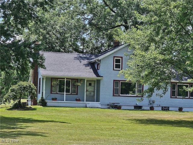 view of front facade featuring roof with shingles, a front lawn, and a chimney