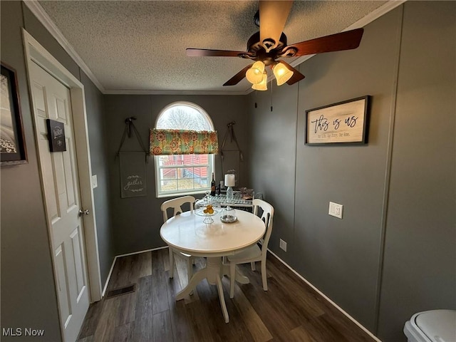 dining room with a textured ceiling, dark wood-style flooring, visible vents, a ceiling fan, and crown molding