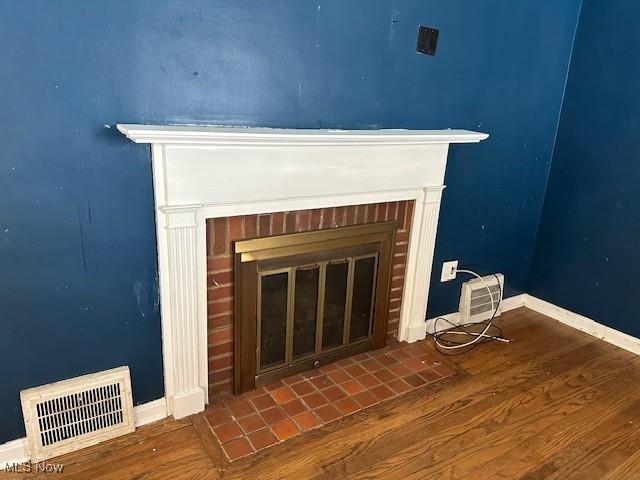 room details with visible vents, a fireplace, baseboards, and wood finished floors