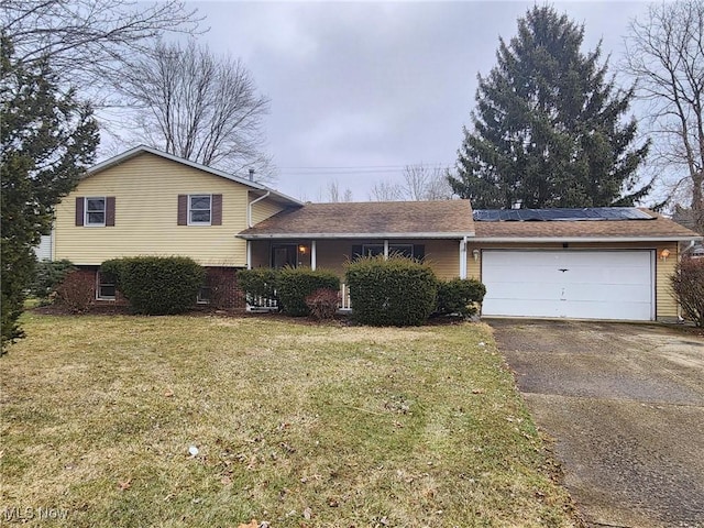 split level home featuring an attached garage, driveway, a front lawn, and solar panels