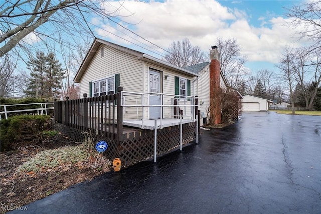 view of property exterior featuring a garage, a chimney, a deck, and an outbuilding