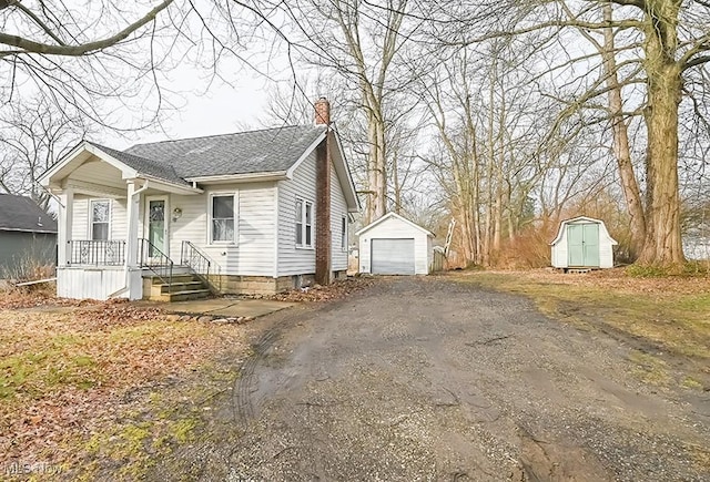 view of front of property with an outbuilding, a shingled roof, a detached garage, driveway, and a chimney