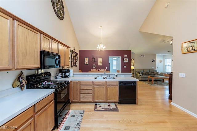 kitchen with light countertops, open floor plan, a sink, a peninsula, and black appliances