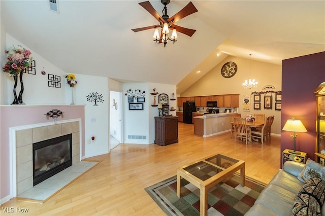 living area with light wood finished floors, ceiling fan with notable chandelier, visible vents, and a tile fireplace