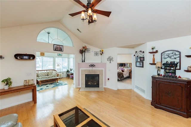 living room with a ceiling fan, a tile fireplace, visible vents, and wood finished floors